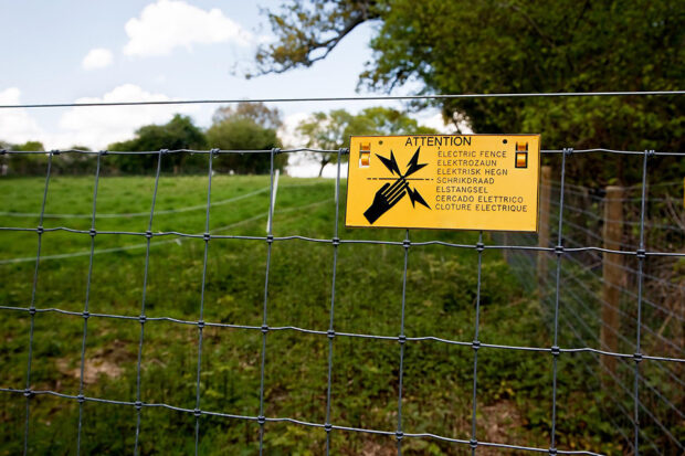 A safety sign on the fence on the edge of a field indicating "Attention Electric Fence"