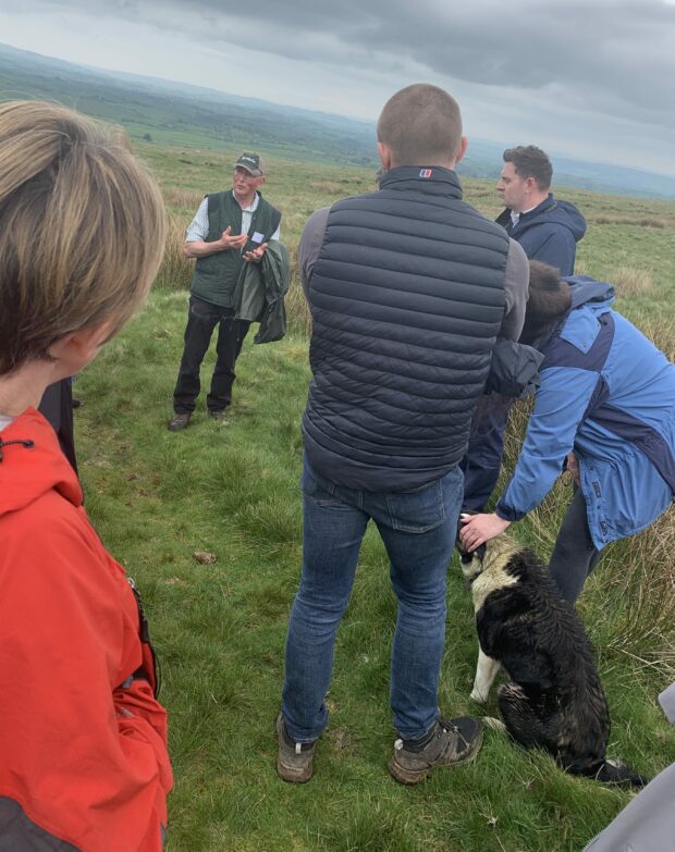 Members of the RPA Customer Board standing in the countryside listening to host farmer talk about his work.