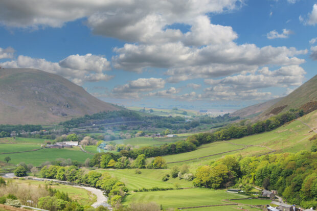 Landscape image of a valley with mountains, a river and fields. 